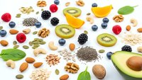Superfood ingredients collection with fresh berries, nuts, seeds, avocado and kiwi arranged on white background for healthy eating and nutrition concepts.