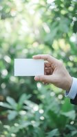 Businessman hand holding blank white business card outdoors with green bokeh nature background, mockup for branding and corporate identity.