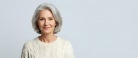 Smiling senior Caucasian woman with gray hair wearing cream cable knit sweater on light background for lifestyle and wellness marketing campaigns.