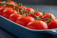 Fresh ripe cherry tomatoes on vine with water drops in blue ceramic serving dish against dark background, macro food photography for culinary use.