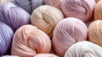 Colorful yarn balls in soft pastel tones including pink, beige, purple and cream arranged together for knitting and crochet crafting projects.