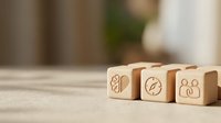 Wooden blocks with business icons including lightbulb, clock and people symbols on desk representing innovation, time management and teamwork concepts.