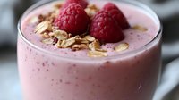 Pink berry smoothie topped with fresh raspberries and granola in glass, healthy breakfast drink with oats and fruit garnish for nutritious morning meal.