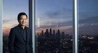 Confident male professional in dark business suit standing by floor-to-ceiling windows overlooking illuminated city skyline at dusk, suitable for corporate leadership and business success concepts.