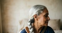 Senior woman with long gray hair braided, fair complexion, wearing dark blue clothing, shown in profile against neutral beige background. Suitable for healthcare, wellness, aging, lifestyle, and senior living concepts.