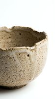 Rustic handmade ceramic bowl with speckled beige glaze and rough textured edges, isolated on white background.