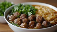 Savory meatball noodle soup with fresh herbs in white bowl, comfort food meal with tender beef balls, cilantro garnish and golden broth for culinary content.
