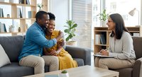 Happy African American couple embracing on couch during therapy session with female counselor in modern office setting for relationship support.