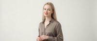 Young blonde Caucasian businesswoman in brown blazer standing confidently against neutral background for corporate presentations and marketing materials.