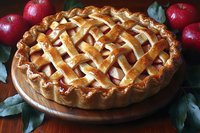 Fresh baked apple pie with golden lattice crust on wooden board, surrounded by red apples and green leaves, showcasing traditional homemade pastry.