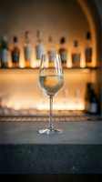 Glass of white wine on bar counter with blurred bottles in background. Elegant stemware in upscale restaurant or cocktail lounge setting for dining concepts.