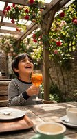 Happy young boy enjoying orange juice at outdoor garden cafe with rose pergola during sunny day celebration.