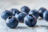 Fresh ripe blueberries with water drops on light marble background, macro shot showing texture and natural organic appearance. For food packaging design.