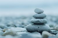Balanced stack of smooth gray stones on pebble beach against blurred blue background creates zen atmosphere for wellness and meditation practices.