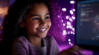 Young African American girl smiling while working on computer at night, illuminated by purple neon lighting. Coding or programming education concept for children.