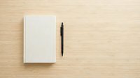 Blank notebook with black pen on wooden desk surface, ready for writing, planning, and creative work projects.
