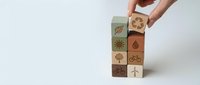 Hand stacking wooden blocks with environmental sustainability icons including renewable energy, recycling, and eco-friendly symbols on white background.