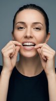 Young woman with dark hair and fair complexion using dental floss for oral hygiene routine against neutral gray background.