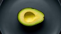 Halved avocado with pit removed on dark plate, fresh green fruit for healthy eating and culinary use.