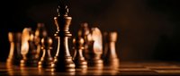 Wooden chess king piece stands prominently on board with blurred pieces in background, symbolizing leadership, strategy and business success concepts.