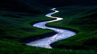 Winding river meandering through lush green valley landscape with rolling hills and vibrant grass meadows creating scenic natural waterway view.