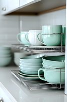 Organized mint green ceramic dishes and cups neatly arranged on chrome wire shelves in modern white kitchen cabinet for storage and home organization.