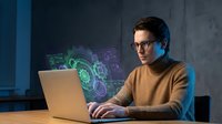 Young professional man working on laptop with holographic digital interface displaying data analytics and futuristic technology in modern office.