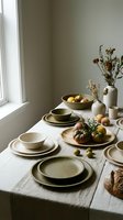 Rustic ceramic dinnerware set with fresh fruits and dried flowers on linen tablecloth near window creating warm natural dining atmosphere for home decor.