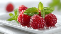 Fresh red raspberries with green mint leaves on white plate, healthy organic berries for desserts, smoothies and summer recipes.