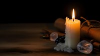 Burning candle with melted wax on wooden table surrounded by old scrolls and vintage items creating atmospheric mood for meditation and relaxation.