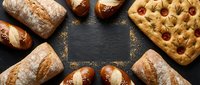 Fresh artisan bread assortment with pretzels and focaccia arranged on dark slate background. Bakery products display for culinary and food service concepts.