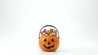 Carved jack-o-lantern pumpkin bucket filled with colorful wrapped candies and treats, isolated on white background for Halloween celebrations and seasonal designs.