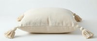 Soft cream linen throw pillow with decorative corner tassels on white background, boho home decor accent for living room styling.