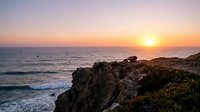 Stunning ocean sunset over rocky coastline with golden sky and gentle waves. Peaceful seascape with rugged cliffs and warm evening light for travel content.