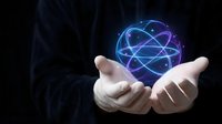 Businessman hands holding glowing blue atomic structure hologram representing nuclear energy, science technology and molecular physics concepts.