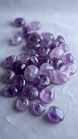 Collection of polished amethyst gemstones in various purple shades scattered on marble surface for jewelry making and crystal healing practices.