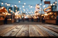 Rustic wooden table with blurred festive market or street fair in background, string lights creating warm bokeh atmosphere.