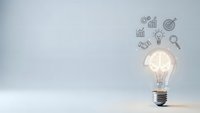 Glowing light bulb with business icons floating above representing innovation, creativity, and strategic planning concepts for corporate presentations.