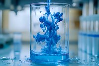 Vibrant blue ink drops dissolving in clear water inside glass beaker, creating dynamic fluid art patterns against laboratory background for creative design projects.