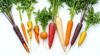 Fresh organic rainbow carrots with green tops isolated on white background for healthy cooking and farm-to-table cuisine preparation.
