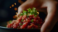 Fresh raw tuna tartare with green onions and sesame seeds on dark plate, selective focus on red fish cubes garnished with herbs. Restaurant appetizer.