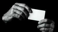 Elderly hands holding blank white business card against dark background in monochrome style for corporate identity and branding projects.