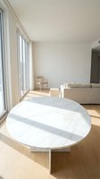 Modern minimalist living room with marble round coffee table, beige sofa and natural sunlight streaming through large windows creating warm atmosphere.