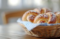 Fresh homemade sweet buns with powdered sugar served in wicker basket with blue checkered napkin on wooden table, selective focus on pastries.