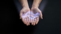 Male hands cupped together holding glowing purple energy light orb against dark background for spiritual healing meditation and wellness concepts.