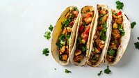 Delicious Mexican tacos with spicy meat filling, fresh vegetables, and herbs served on white plate for food photography or restaurant menu.