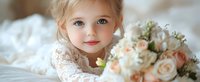 Young girl in white lace dress holding elegant bouquet of pink and white roses, lying on soft bedding with dreamy expression, natural light portrait for wedding or special occasion.