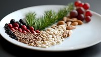 Fresh ingredients arranged in decorative wave pattern on white plate with nuts, seeds, berries, grapes and herbs creating modern food composition for healthy eating concept.