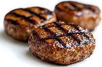 Juicy grilled beef patties with classic char marks and seasoning on white background, close-up view showing texture and caramelization for food marketing.