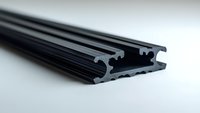 Black aluminum extrusion profile on light background, industrial metal construction detail with complex cross-section shape for manufacturing and engineering.